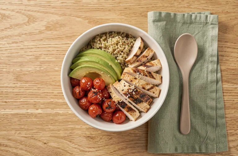 Bol repas équilibré vue de dessus avec quinoa, avocat, tomates rôties et poulet grillé sur table en bois naturel